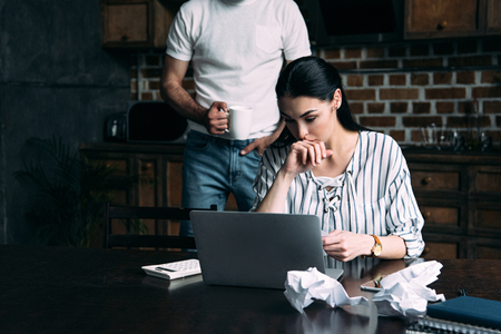 stressed young woman counting bills while her husband standing behindの写真素材