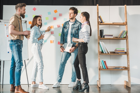 Successful business people discussing ideas by white board with sticky notes in modern light officeの写真素材