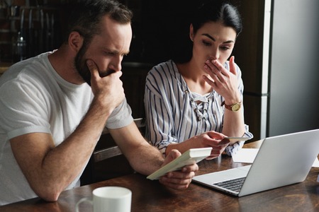 depressed young couple counting tax and bills with laptop and calculatorの写真素材