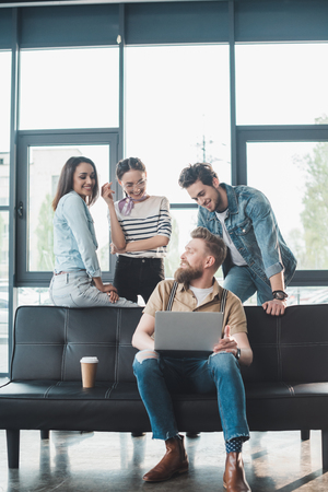 Businessman and women looking at their male colleague working on laptop in modern officeの写真素材