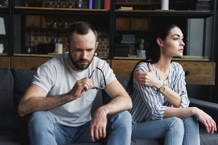 sad couple sitting on sofa at home after quarrel and looking away