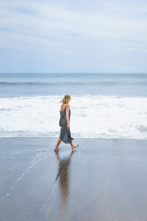back view of blonde girl in long dress walking near seaの写真素材