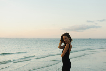 beautiful woman in dress posing on ocean beach during sunsetの写真素材