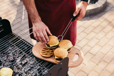 Chef adjusting bun on meat of burgers cooked outdoors on grillの写真素材