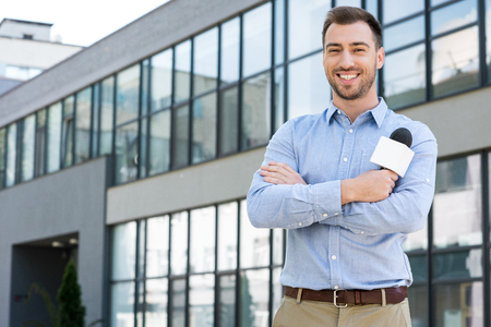 cheerful male journalist posing with microphone outsideの写真素材