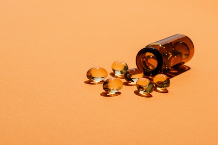 close-up shot of transparent yellow pills spilled from bottle on orange surfaceの写真素材