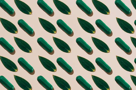top view of phytotherapy pills with green leaves in rows pattern on beige surfaceの写真素材