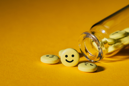 close-up shot of pills with smiley faces and glass bottle on yellowの写真素材