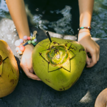 partial view of young woman holding fresh coconut cocktail at swimming poolの写真素材