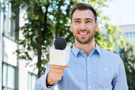 smiling male journalist taking interview with microphoneの写真素材
