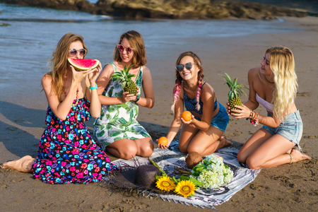 group of happy young women with fruits sitting together on beachの写真素材