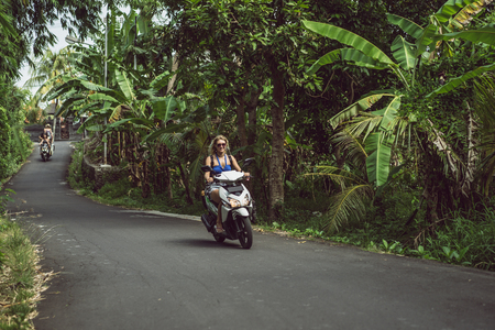 girls riding motorcycles on road between tropical plantsの写真素材