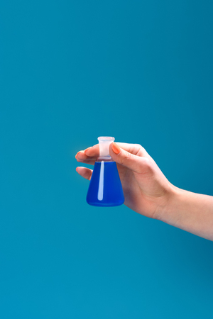 cropped shot of woman holding flask of blue liquid isolated on blue