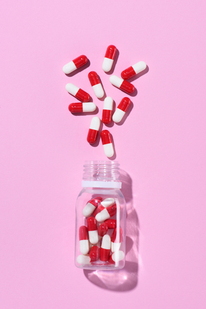 top view of red pills spilled from plastic jar on pinkの写真素材