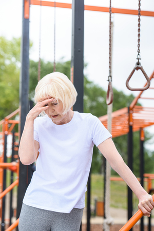 senior tired sportswoman standing on sports groundの写真素材