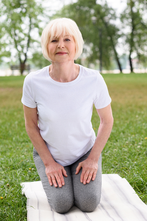 senior woman practicing yoga on mat on green lawnの写真素材
