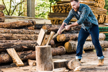 lumberjack in checkered shirt chopping log at sawmillの写真素材