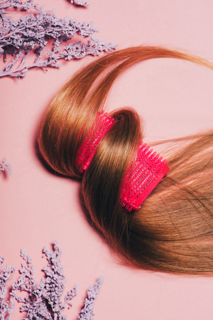 top view of hair rolled over curler with flowers on pink surfaceの写真素材