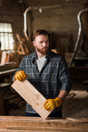 carpenter in protective gloves working with wooden plank at sawmillの写真素材