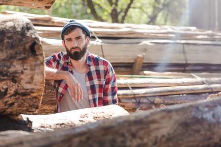 bearded lumberjack in checkered shirt standing at sawmillの写真素材
