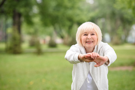 elderly sportswoman exercising on green lawn in parkの写真素材