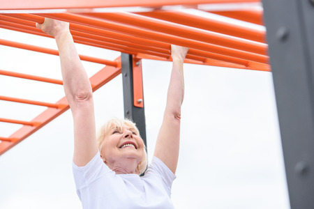 smiling elderly woman exercising on sports ground