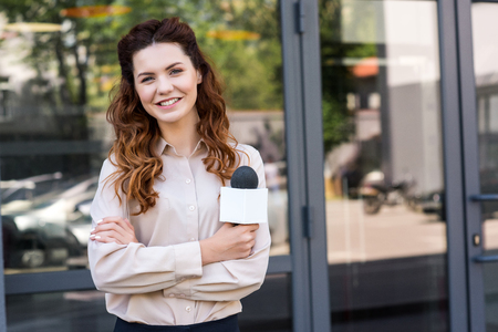 attractive female journalist holding microphone and looking at cameraの写真素材