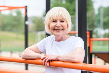 smiling senior woman standing on sports ground and looking at cameraの写真素材