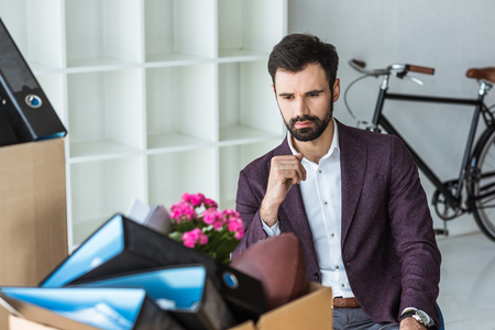fired young businessman sitting in office and looking at box of personal stuffの写真素材
