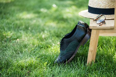 close up view of arrangement of eyeglasses, black shoes and hat on wooden stairs on green grassの写真素材