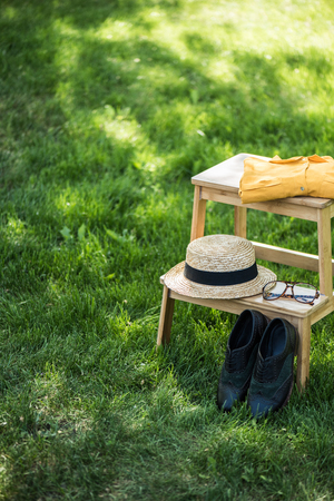 close up view of arrangement of eyeglasses, black shoes, shirt and hat on wooden stairs on green grassの写真素材