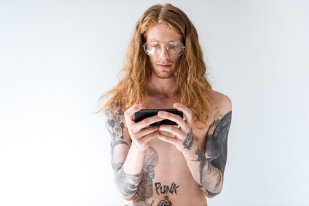 handsome shirtless tattooed man with curly hair using smartphone isolated on whiteの写真素材