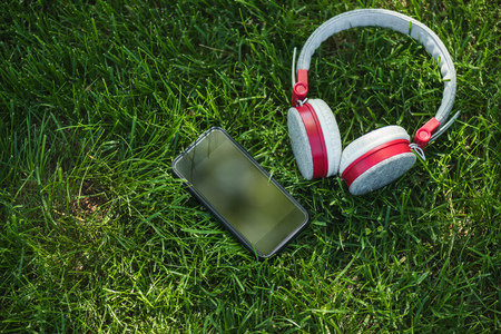 close up view of smartphone with  blank screen and headphones on green grass