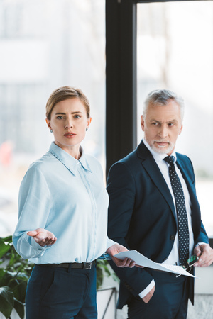 senior businessman looking at businesswoman holding papers and looking at cameraの写真素材