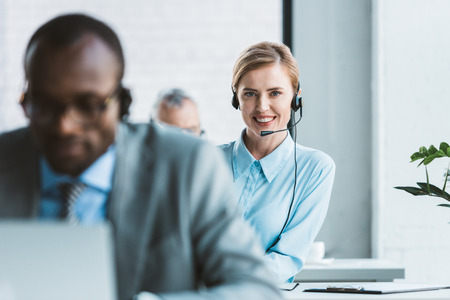 selective focus of attractive businesswoman in headset smiling at camera