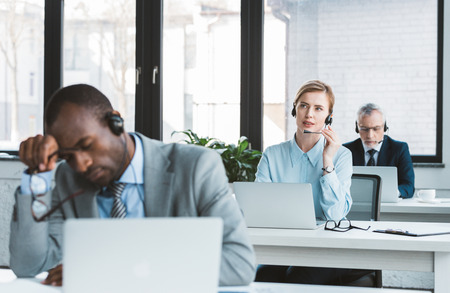 three multiethnic business people in headsets working with laptops in modern officeの写真素材