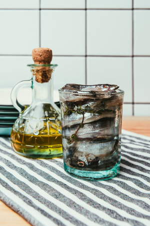 Front view of pile of salted fish in glass on towel with bottle of oil and plates behindの写真素材