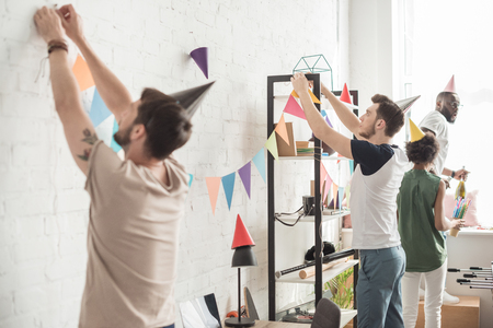 young men hanging up string with party garlands and their friends standing behindの写真素材