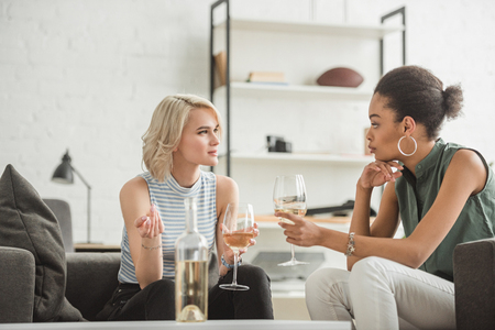 multiethnic young women sitting and talking with glasses of white wineの写真素材