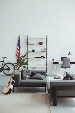 interior of modern living room with bicycle, guitar, american flag, laptop, shelves and armchairsの写真素材