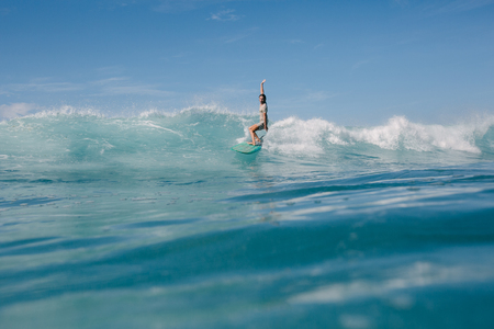 young man riding blue ocean waves on surfboard on sunny dayの写真素材