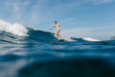 handsome man in wet t-shirt riding waves on surfboard on sunny dayの写真素材