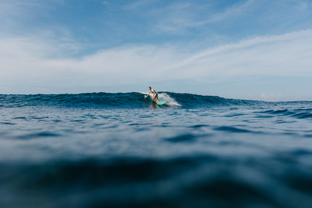 handsome man riding blue ocean waves on surfboardの写真素材