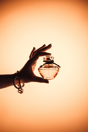 cropped view of female hand with sensual perfume in translucent bottle, isolated on yellowの写真素材