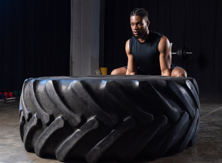 athletic african american man exercising with tyre and looking away in gymの写真素材