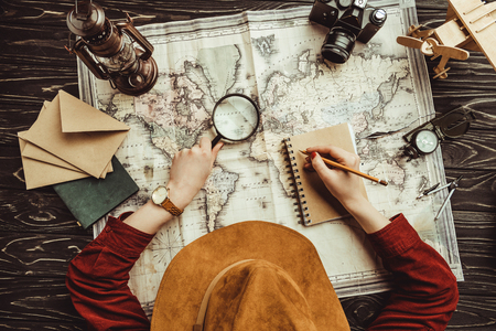overhead view of woman making notes in notebook with blank envelopes, map and photo camera on wooden surfaceの写真素材