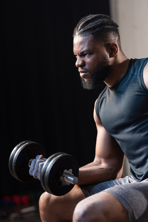 serious african american sportsman exercising with dumbbell and looking awayの写真素材