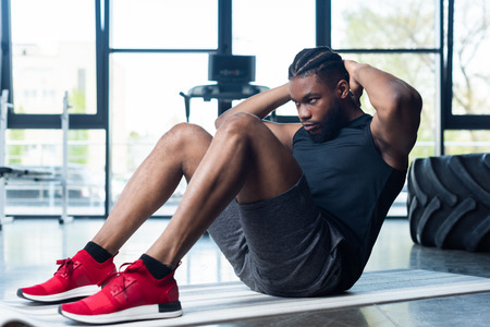 athletic young african american man doing abs and looking away in gymの写真素材