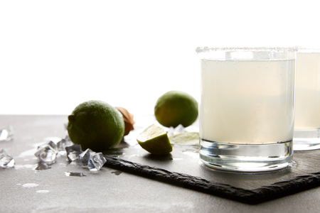 Close up view of refreshing margarita cocktails with lime on tabletop on white