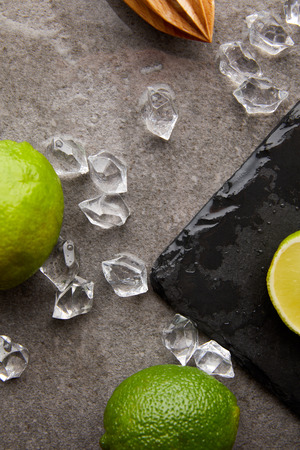 flat lay with wooden squeezer, limes and ice cubes for cocktail on grey surfaceの写真素材